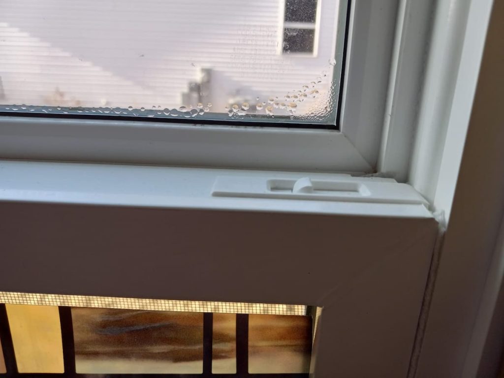 Condensation concentrated at the corner of a vinyl window frame during Wisconsin winter — the solid structural corner conducts cold more directly than the hollow frame sections