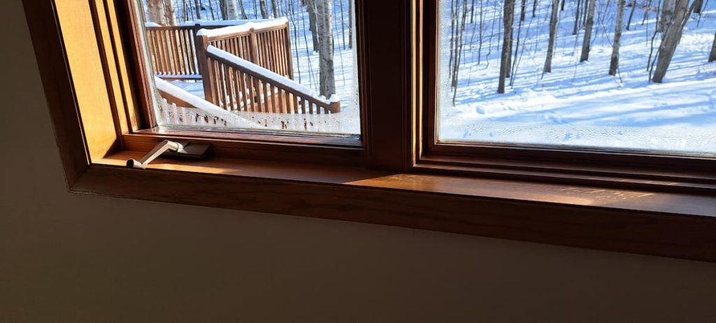 Winter window condensation on wood frame windows with snowy scene outside — condensation affects both wood and non-wood windows when indoor humidity is too high